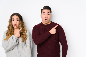 Young couple posing in a white background pointing to the side