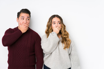 Young couple posing in a white background thoughtful looking to a copy space covering mouth with hand.