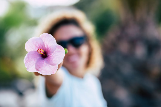 Spring and happiness concept with happy cheerful defocused woman showing a big pink flower with hand smiling and playing in front of the camera - beauty and freshness with adult people outdoor