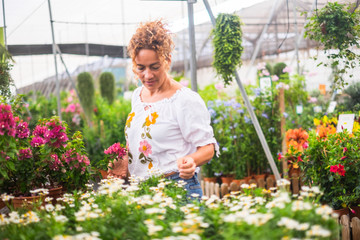 Gardening activity with beautiful adult woman in the middle of a flowers and plants store shop business place - people enjoying green. healthy nature and coloured flower