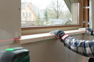 home improvement handyman installing window sill in new build attic by using leveler and laser...