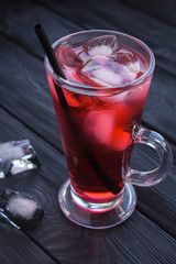 Iced hibiscus or karkade tea in the glass on the black wooden  background. Location vertical. Closeup.
