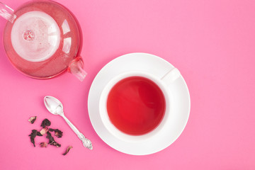 Fototapeta na wymiar Hibiscus or karkade tea in the white cup and glass teapot on the pink background. Top view. Copy space.