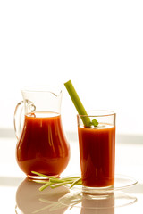 Tomato juice in a jug and a glass with celery, on a white background, close-up