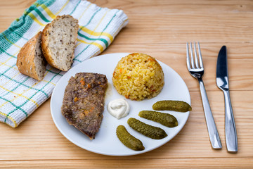 Prepared beef steak with rice risotto, pickles and sauce on white plate on wooden table background