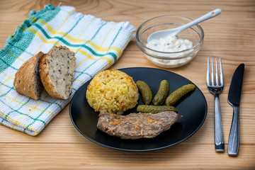 Prepared beef steak with rice risotto, pickles and sauce on black plate on wooden table background