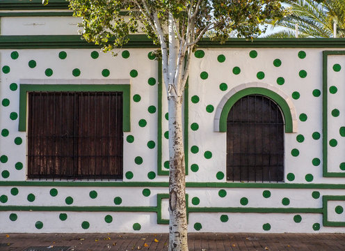 fachada con dos ventanas de madera lunares verdes y &aacute;rbol delante