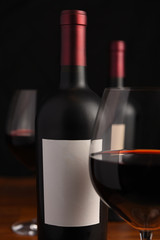 Closeup of a red wine bottle with blank label and out of focus wine glasses  in foreground and background.