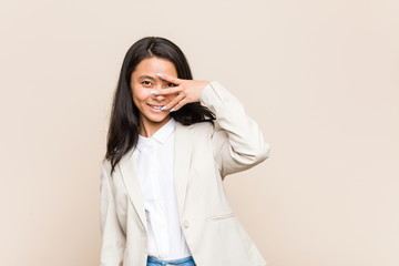 Young business chinese woman blink at the camera through fingers, embarrassed covering face.