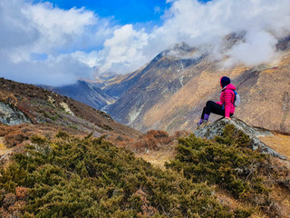 Fototapeta premium Everest base camp trek itinerary: way from Phortse Tanga to Dole, Solokhumbu, Nepal. Beautiful view on the valley on a cloudy day. A trekker having rest on the hill and observing great scenery.
