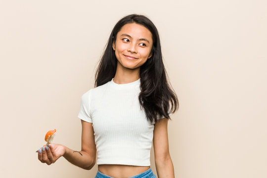 Young asian woman holding a sushi piece smiling confident with crossed arms.