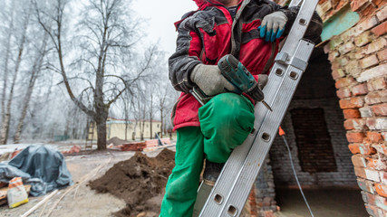 Worker in protect gloves is holding the hand screwdriver on the ladder in construction site....