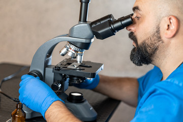 Male laboratory assistant examining biomaterial samples in a microscope