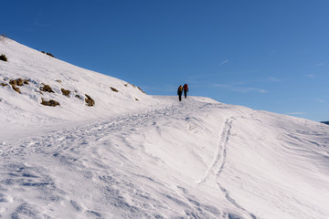 Fototapeta na wymiar Personen auf Weg im Schnee in den Alpen vor blauem Himmel