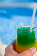 Vacation and rest concept. A man holds in his hand glass with colorful cocktail with drinking straw over the palm trees. Selective focus.