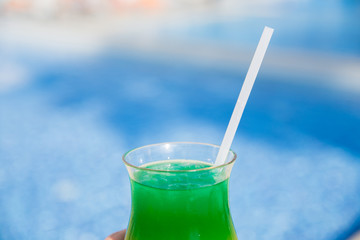 Vacation and rest concept. A man holds in his hand glass with colorful cocktail with drinking straw over the palm trees. Selective focus.