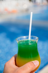 Vacation and rest concept. A man holds in his hand glass with colorful cocktail with drinking straw over the palm trees. Selective focus.