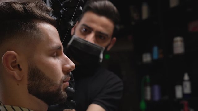Barber correcting shape of client's eyebrows with thread