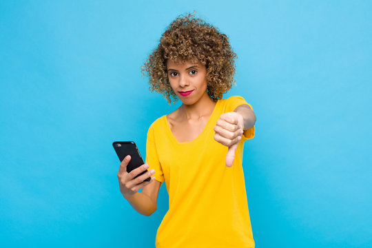 Young African American Feeling Cross, Angry, Annoyed, Disappointed Or Displeased, Showing Thumbs Down With A Serious Look With A Mobile Phone