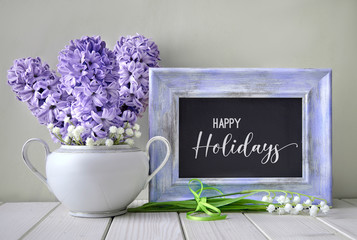 Blue springtime background. Light purple hyacinth and lily of the valley flowers around blackboard in violet frame. Text 