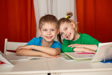 funny cute children of 8-9 years old laugh, schoolchildren do homework at the table, red background