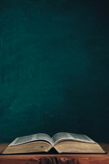 Open bible on a red old wooden table. Beautiful green wall background.