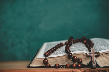 Close up Open Holy Bible and beads crucifix on a red old wooden table. Beautiful green wall...