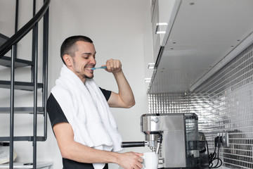 A young guy is going to work in the morning. Brushes teeth near a coffee machine while waiting for a cup of coffee