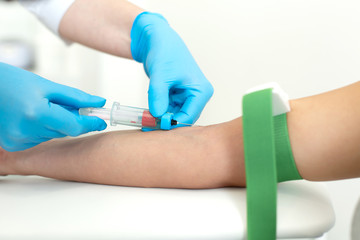 a gloved nurse inserts a needle into a vein on the patient arm and draws blood into a vacuum...