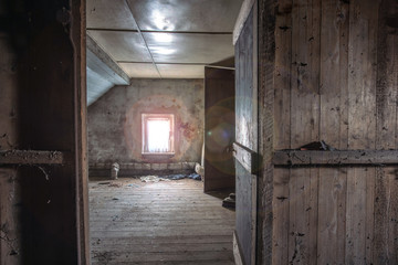 Fototapeta na wymiar Old wooden dark abandoned attic with sunlight through the window and a open door, needs renovation