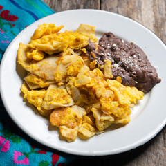 Mexican scrambled eggs with corn tortilla also called migas on wooden background