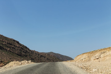 Fototapeta na wymiar Empty road in southern Morocco with blue skies and mountains in the background