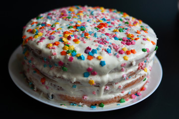 Beautiful cake with white cream and colored topping Cake standing on the table, isolated on a black background. Horizontal color photo.