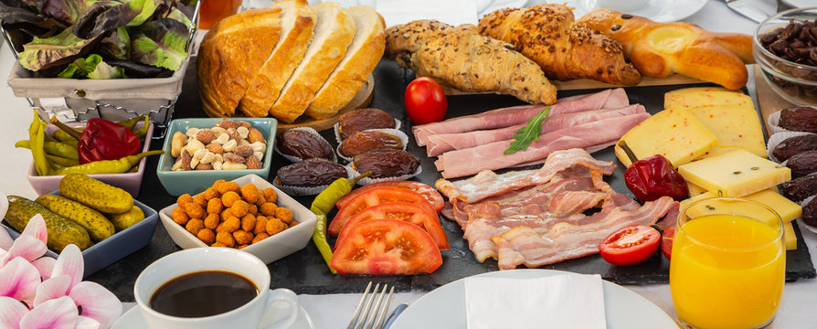 Breakfast on the table. Croissant bread, Croissant cereal, Bacon, ham, cheese, lettuce, beans, cornflakes, fruit, coffee, tea, and orange juice is breakfast. , Lunch or dinner for every day