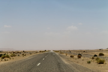 Empty road in southern Morocco with blue skies and mountains in the background