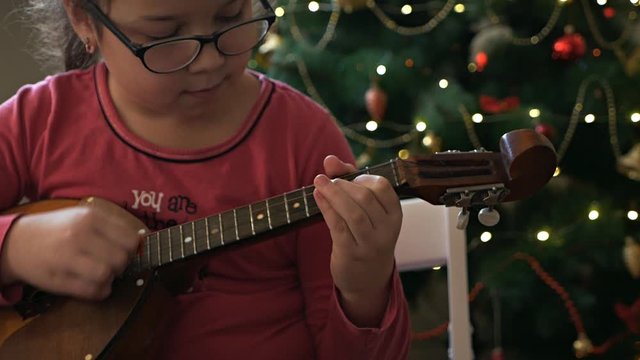 Girl plays dombra against the background of a decorated, Christmas tree