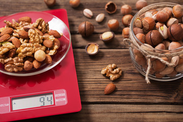 mix of different nuts on  kitchen scale on old wooden background