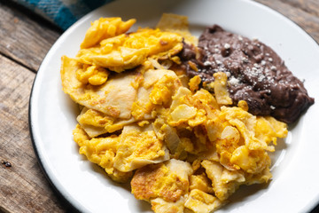 Mexican scrambled eggs with corn tortilla also called migas on wooden background