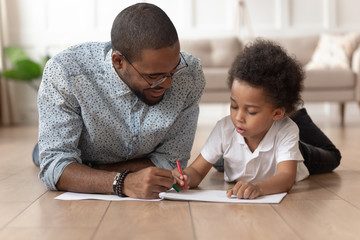 Black man with little son lying on floor, drawing pictures.