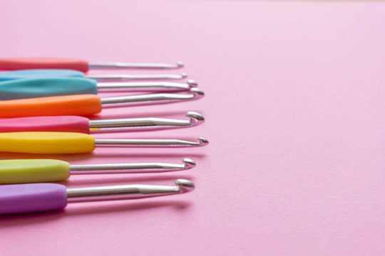Closeup image of different size colorful crochet hooks on soft pink background