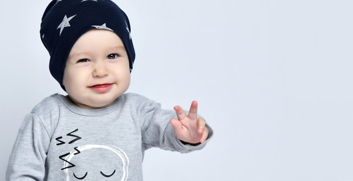 Little baby boy toddler in grey casual jumpsuit, black cap with starssmiling and gesticulating