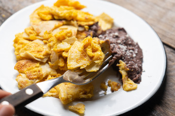Mexican scrambled eggs with corn tortilla also called migas on wooden background
