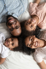 Happy black family laying head to head on bed.