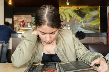 Mujer joven morena lee el menú en un restaurante