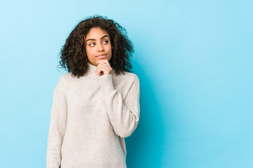 Young african american curly hair woman looking sideways with doubtful and skeptical expression.