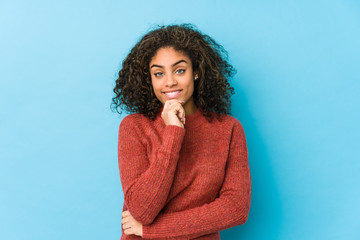 Young african american curly hair woman smiling happy and confident, touching chin with hand.