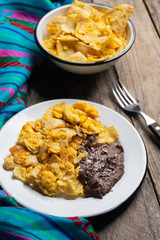 Mexican scrambled eggs with corn tortilla also called migas on wooden background