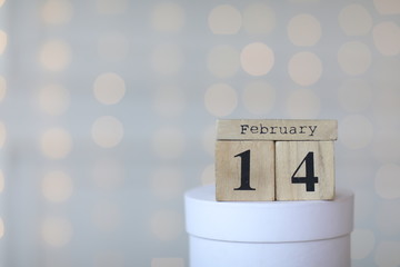 Valentine's day concept. Date 14 February on wooden red cube calendar on a white gift box. Bokeh golden and white background.