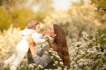 A beautiful young, happy woman with a baby in the spring in a blooming garden, smiling and tossing the baby. Concept: spring. Mother's day. Relationships in the family. March 8.