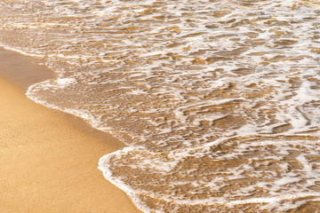 Sea wave on yellow sand beach. Seawater and foam. Sunny beach